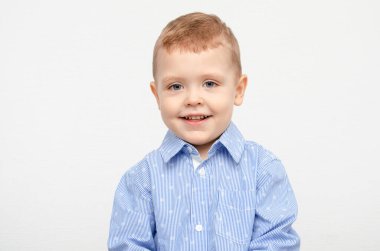 Beyaz arka planda mavi gömlekli şirin bir çocuk gülümsüyor. Tatil için giyinmiş ve budanmış zarif bir bebek.