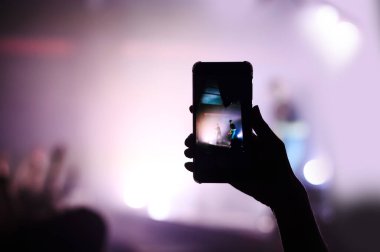 Konserdeki kalabalıktan gelen el hafızası için akıllı telefondan video çekiyor.
