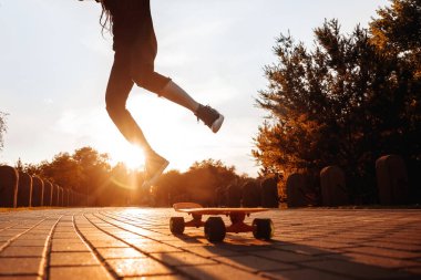 Parkta batan güneşin altında kaykay üzerinde zıplayan bir kızın silueti. Rastalı ve güneş gözlüklü hippi uzun tahta üzerinde numaralar öğreniyor..