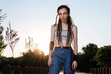 Kot pantolonlu ince saçlı ve gün batımında sörf tahtasına binen bir kız. Güzel genç kız kaykaycı. yaz tatili