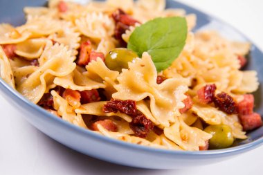 Farfalle makarna güneş ile kurutulmuş domates, jambon ve taze nane ile dekore edilmiş zeytin