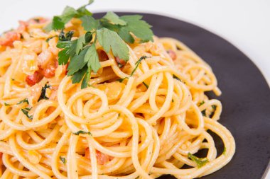 Spagetti Carbonara beyaz bir arka plan üzerinde siyah bir plaka üzerinde bazı maydanoz ile