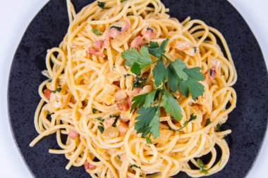 Spagetti Carbonara beyaz bir arka plan üzerinde siyah bir plaka üzerinde bazı maydanoz ile