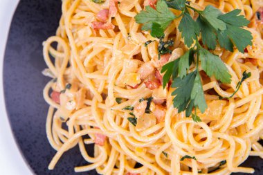 Spagetti Carbonara beyaz bir arka plan üzerinde siyah bir plaka üzerinde bazı maydanoz ile