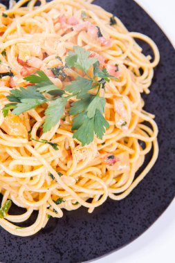 Spagetti Carbonara beyaz bir arka plan üzerinde siyah bir plaka üzerinde bazı maydanoz ile