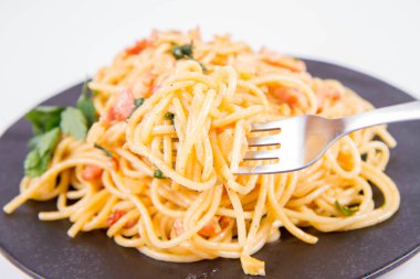 Spagetti Carbonara çatalla yenmekten beyaz bir arka plan üzerinde siyah bir plaka üzerinde bazı maydanoz ile