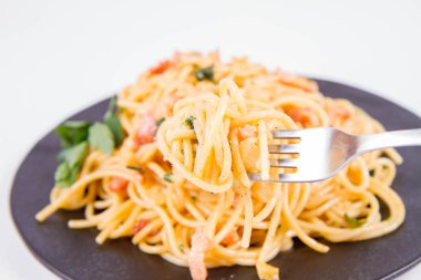 Spagetti Carbonara çatalla yenmekten beyaz bir arka plan üzerinde siyah bir plaka üzerinde bazı maydanoz ile