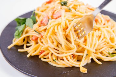 Spagetti Carbonara çatalla yenmekten beyaz bir arka plan üzerinde siyah bir plaka üzerinde bazı maydanoz ile