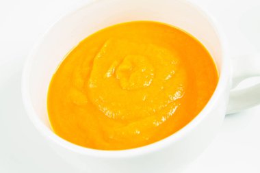 Beyaz arka planda bir kasede balkabağı çorbası