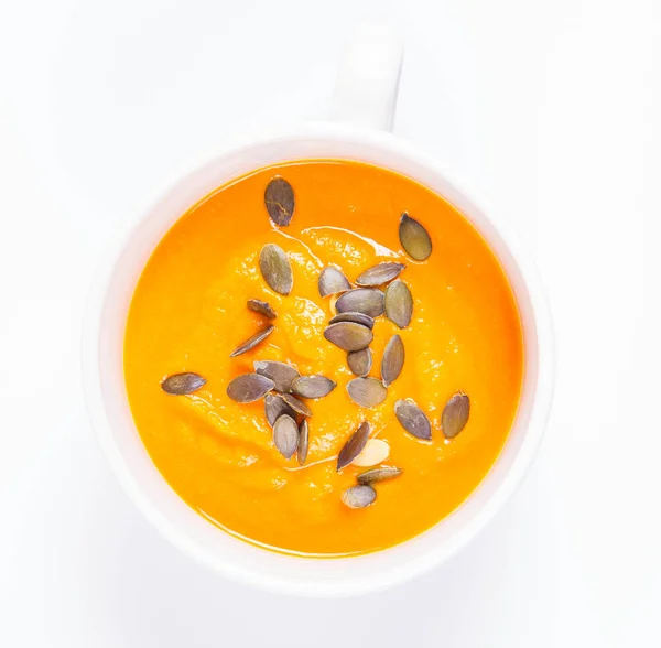Pumpkin soup decorated with pumpkin seeds in a bowl on a white background