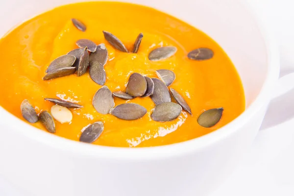 Pumpkin soup decorated with pumpkin seeds in a bowl on a white background