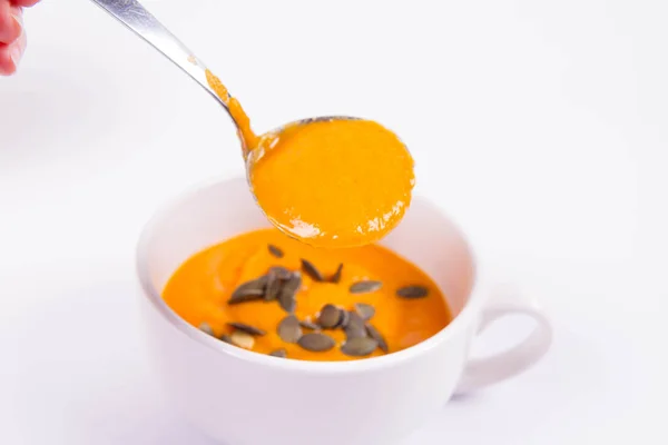 白い背景の上にボウルに注がれているかぼちゃの種で飾られたカボチャのスープ — ストック写真