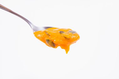 Bir kaşık beyaz bir arka plan üzerinde kabak çekirdeği ile dekore edilmiş balkabağı çorbası