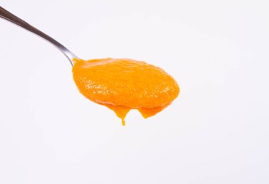 Bir kaşık beyaz bir arka plan üzerinde balkabağı çorbası