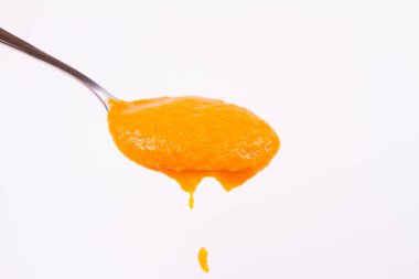 Bir kaşık beyaz bir arka plan üzerinde balkabağı çorbası