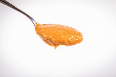 Bir kaşık beyaz bir arka plan üzerinde balkabağı çorbası