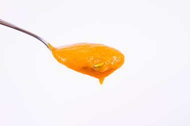 Bir kaşık beyaz bir arka plan üzerinde balkabağı çorbası