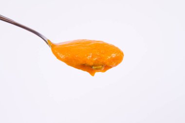 Bir kaşık beyaz bir arka plan üzerinde balkabağı çorbası