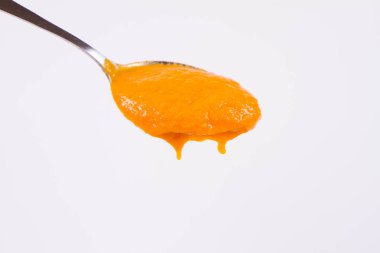 Bir kaşık beyaz bir arka plan üzerinde balkabağı çorbası