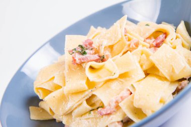 Beyaz zemin üzerinde mavi bir tabakta pappardelle Carbonara