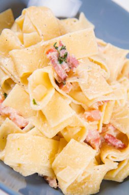 Beyaz zemin üzerinde mavi bir tabakta pappardelle Carbonara