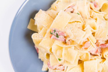 Beyaz zemin üzerinde mavi bir tabakta pappardelle Carbonara