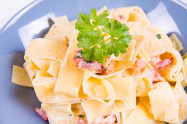 Pappardelle Carbonara beyaz zemin üzerinde mavi bir plaka üzerinde bazı maydanoz ile