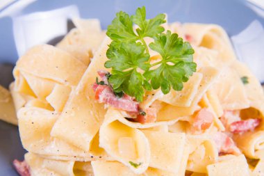 Pappardelle Carbonara beyaz zemin üzerinde mavi bir plaka üzerinde bazı maydanoz ile