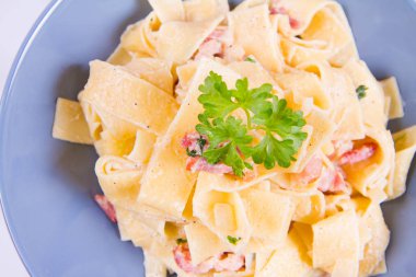 Pappardelle Carbonara beyaz zemin üzerinde mavi bir plaka üzerinde bazı maydanoz ile