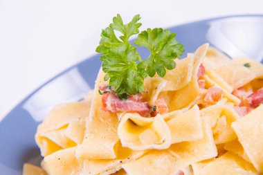 Pappardelle Carbonara beyaz zemin üzerinde mavi bir plaka üzerinde bazı maydanoz ile