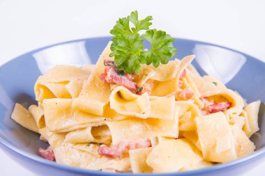 Pappardelle Carbonara beyaz zemin üzerinde mavi bir plaka üzerinde bazı maydanoz ile
