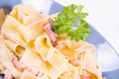 Pappardelle Carbonara beyaz zemin üzerinde mavi bir plaka üzerinde bazı maydanoz ile