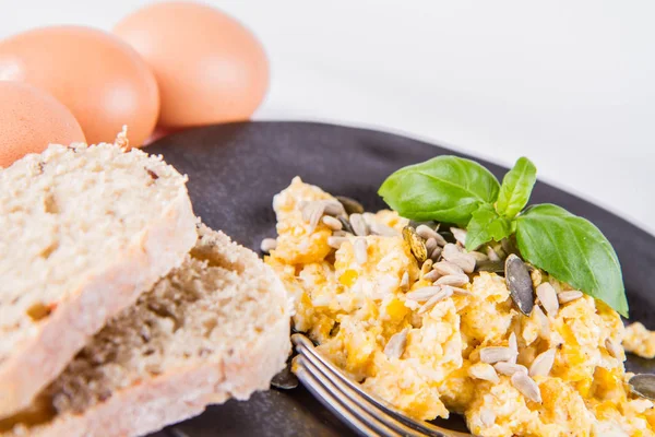 在白色背景上 用叉子用叉子装饰的炒鸡蛋和葵花籽 一些新鲜鸡蛋和全麦面包 — 图库照片