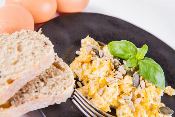 バジル 白の背景に飾られたヒマワリやカボチャの種 いくつかの新鮮な卵と フォークで食べる全粒粉のパンとスクランブルエッグ — ストック写真