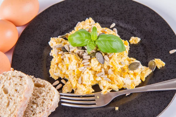 在白色背景上 用叉子用叉子装饰的炒鸡蛋和葵花籽 一些新鲜鸡蛋和全麦面包 — 图库照片