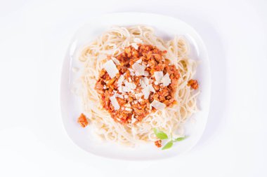 Beyaz arka planda parmesan peyniri ve taze fesleğen ile süslenmiş bir tabakta spagetti bolonez