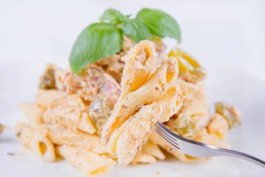 Çatalla yenen makarna. Beyaz krema soslu pastırma ve taze fesleğenle süslenmiş biberli makarna.