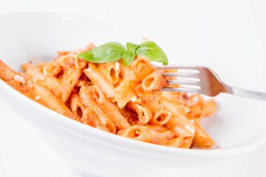 Pesto soslu makarna ve çatalla yenmiş fesleğenle süslenmiş kurutulmuş domates.