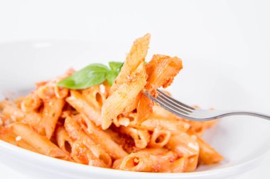 Pesto soslu makarna ve çatalla yenmiş fesleğenle süslenmiş kurutulmuş domates.