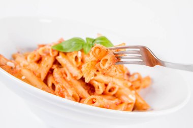 Pesto soslu makarna ve çatalla yenmiş fesleğenle süslenmiş kurutulmuş domates.