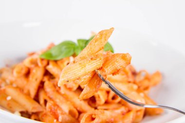 Pesto soslu makarna ve çatalla yenmiş fesleğenle süslenmiş kurutulmuş domates.