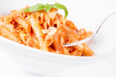 Pesto soslu makarna ve çatalla yenmiş fesleğenle süslenmiş kurutulmuş domates.