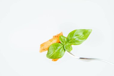 Pesto soslu makarna ve çatalla yenmiş fesleğenle süslenmiş kurutulmuş domates.