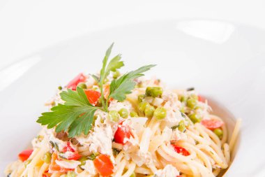 Krema soslu spagetti tütsülenmiş uskumru, bezelye, dolma biber ve beyaz bir tabakta maydanoz.