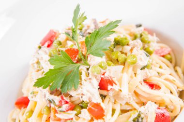 Krema soslu spagetti tütsülenmiş uskumru, bezelye, dolma biber ve beyaz bir tabakta maydanoz.