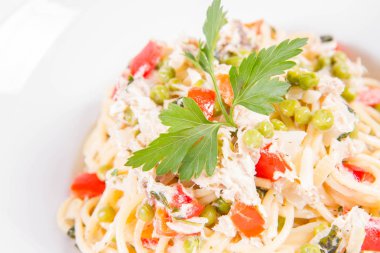 Krema soslu spagetti tütsülenmiş uskumru, bezelye, dolma biber ve beyaz bir tabakta maydanoz.