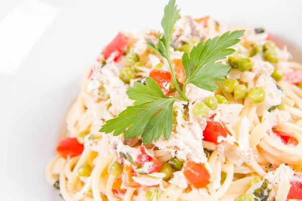 Krema soslu spagetti tütsülenmiş uskumru, bezelye, dolma biber ve beyaz bir tabakta maydanoz.