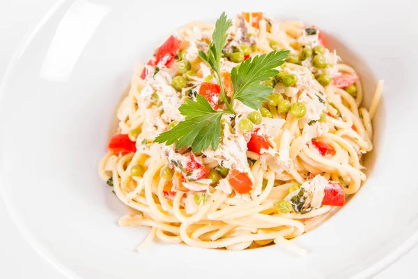 Krema soslu spagetti tütsülenmiş uskumru, bezelye, dolma biber ve beyaz bir tabakta maydanoz.