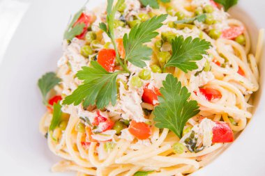 Krema soslu spagetti tütsülenmiş uskumru, bezelye, dolma biber ve beyaz bir tabakta maydanoz.