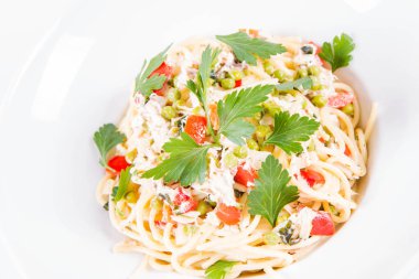 Krema soslu spagetti tütsülenmiş uskumru, bezelye, dolma biber ve beyaz bir tabakta maydanoz.